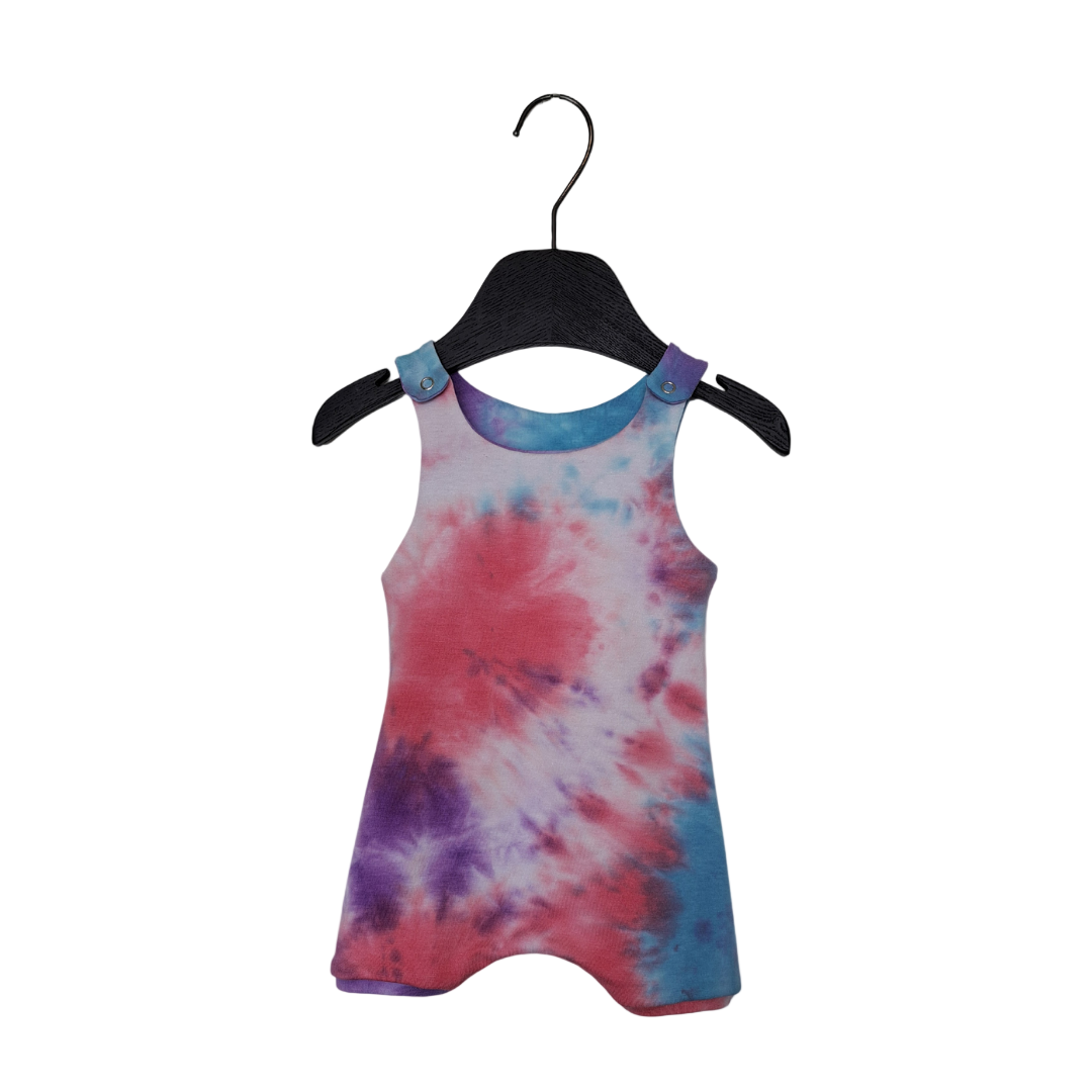 A tie-dye romper for kids, featuring pink and purple shades, with shoulder straps and a snap fastening.