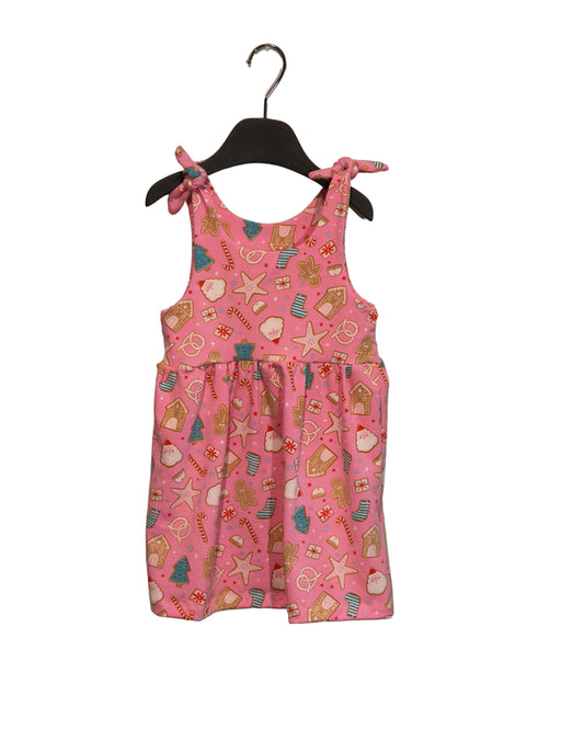 Pink children's dress with pattern on a hanger against a beige wall